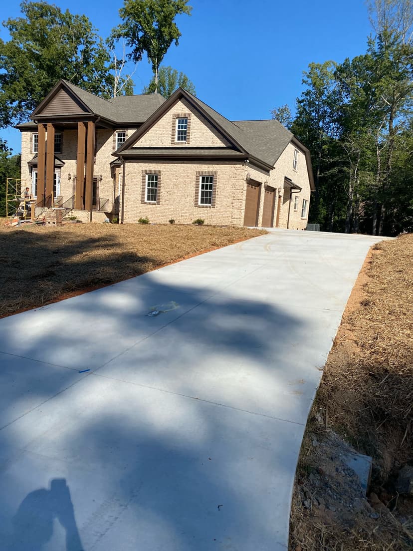 Newly constructed brick home with concrete driveway and landscaped yard in a wooded area.