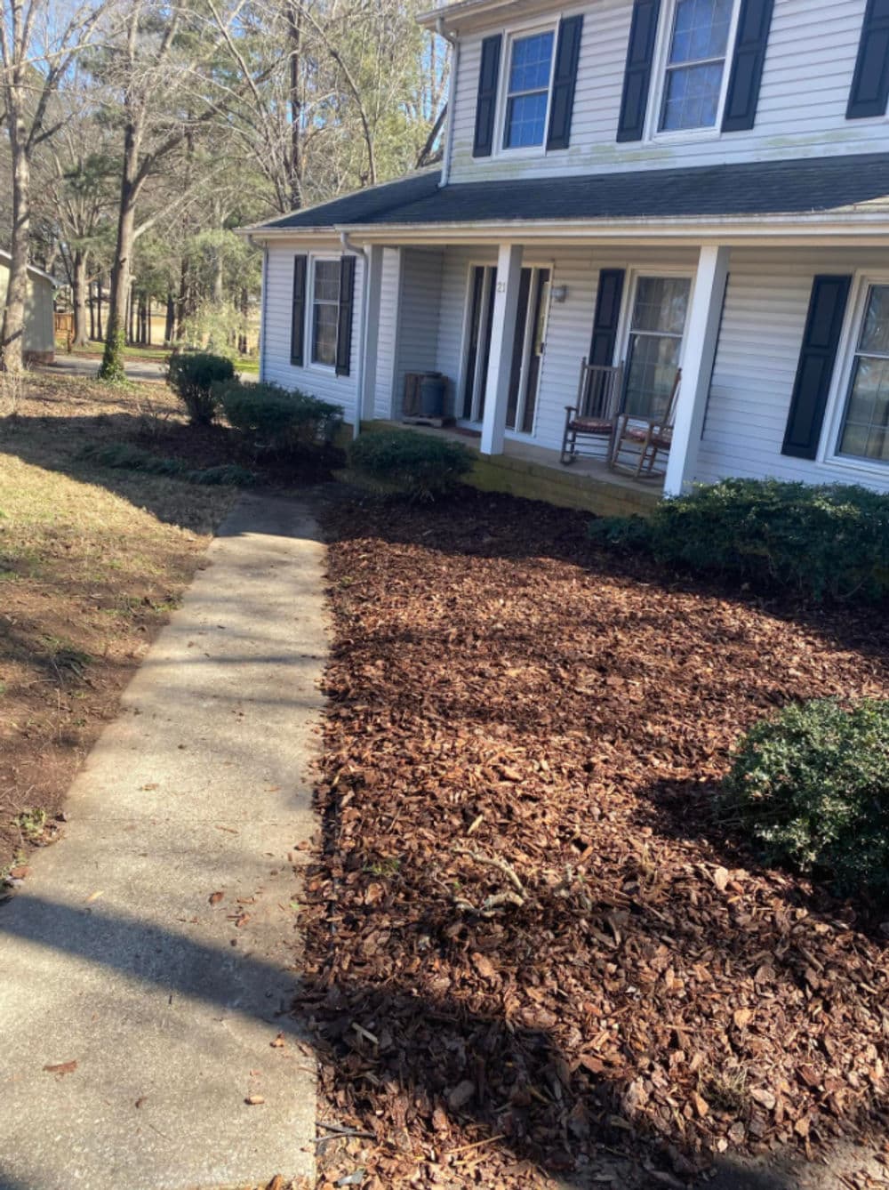 Front yard of a house with a concrete path, landscaped with mulch and greenery.