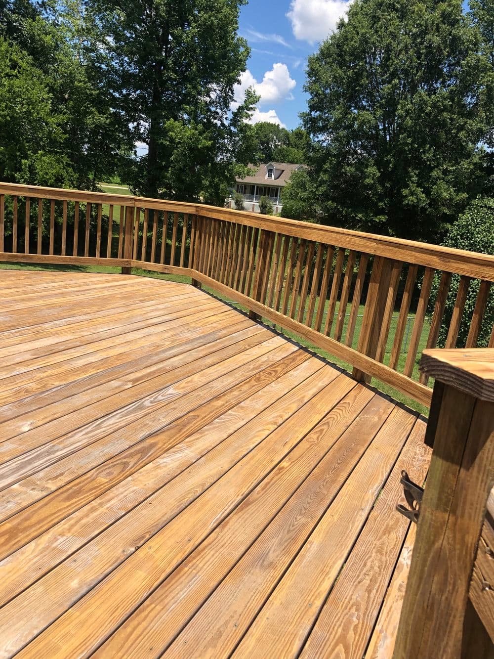 Spacious wooden deck under blue sky with trees, showcasing well-maintained outdoor space.