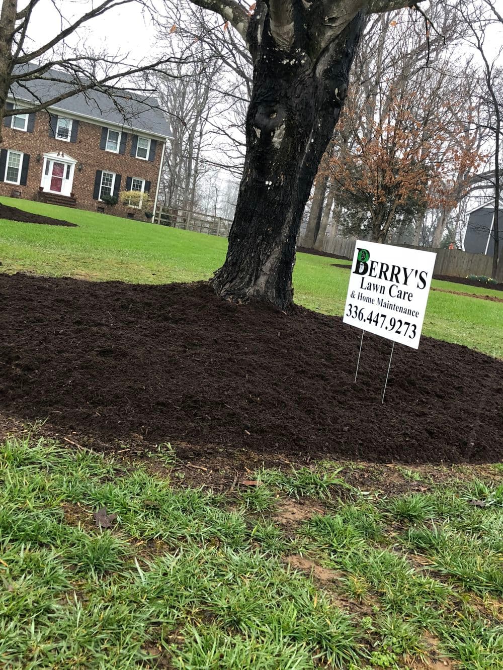 Mulched tree bed with Berry's Lawn Care sign in a well-maintained yard.
